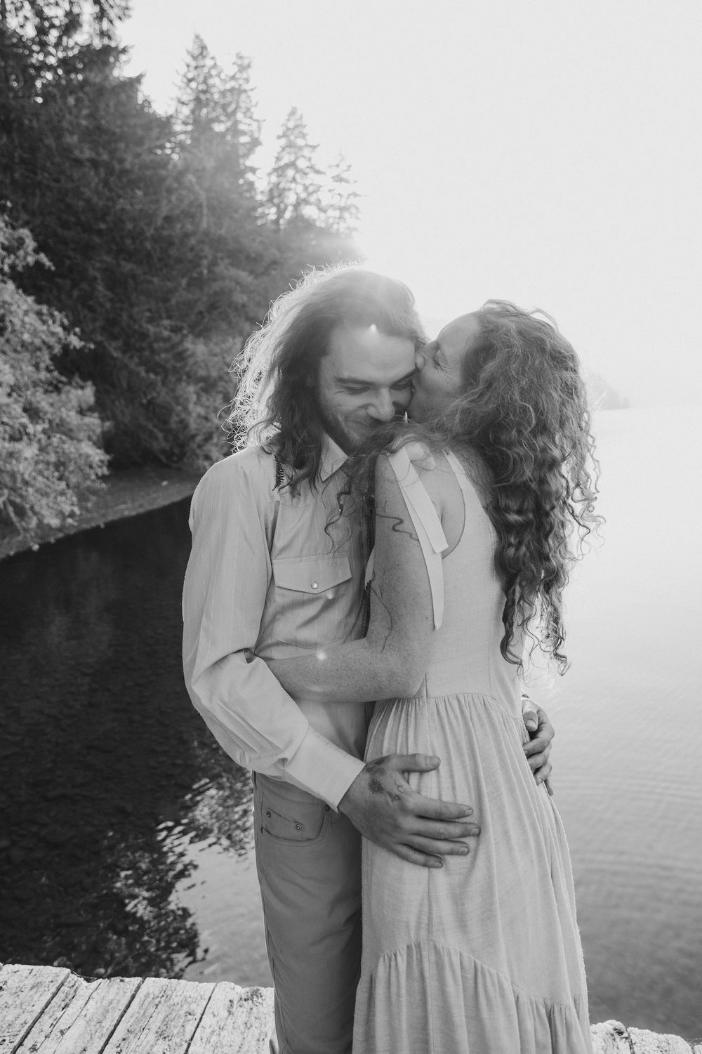 Black and white romantic portrait of a couple in vintage-inspired clothing by the water.