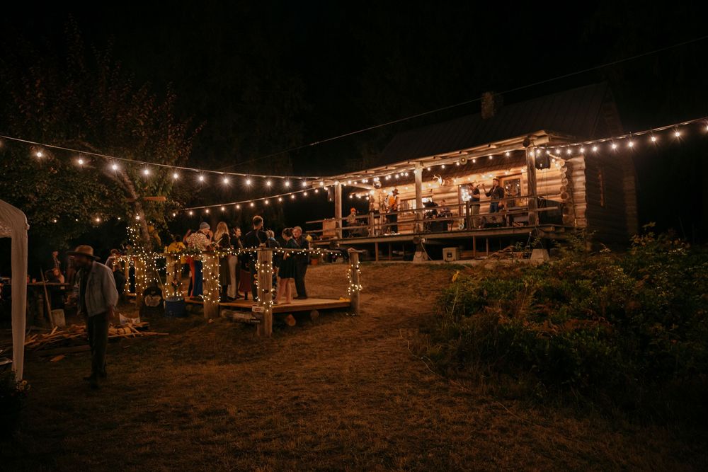 Rustic outdoor venue at night illuminated by string lights with a wooden building in the background.
