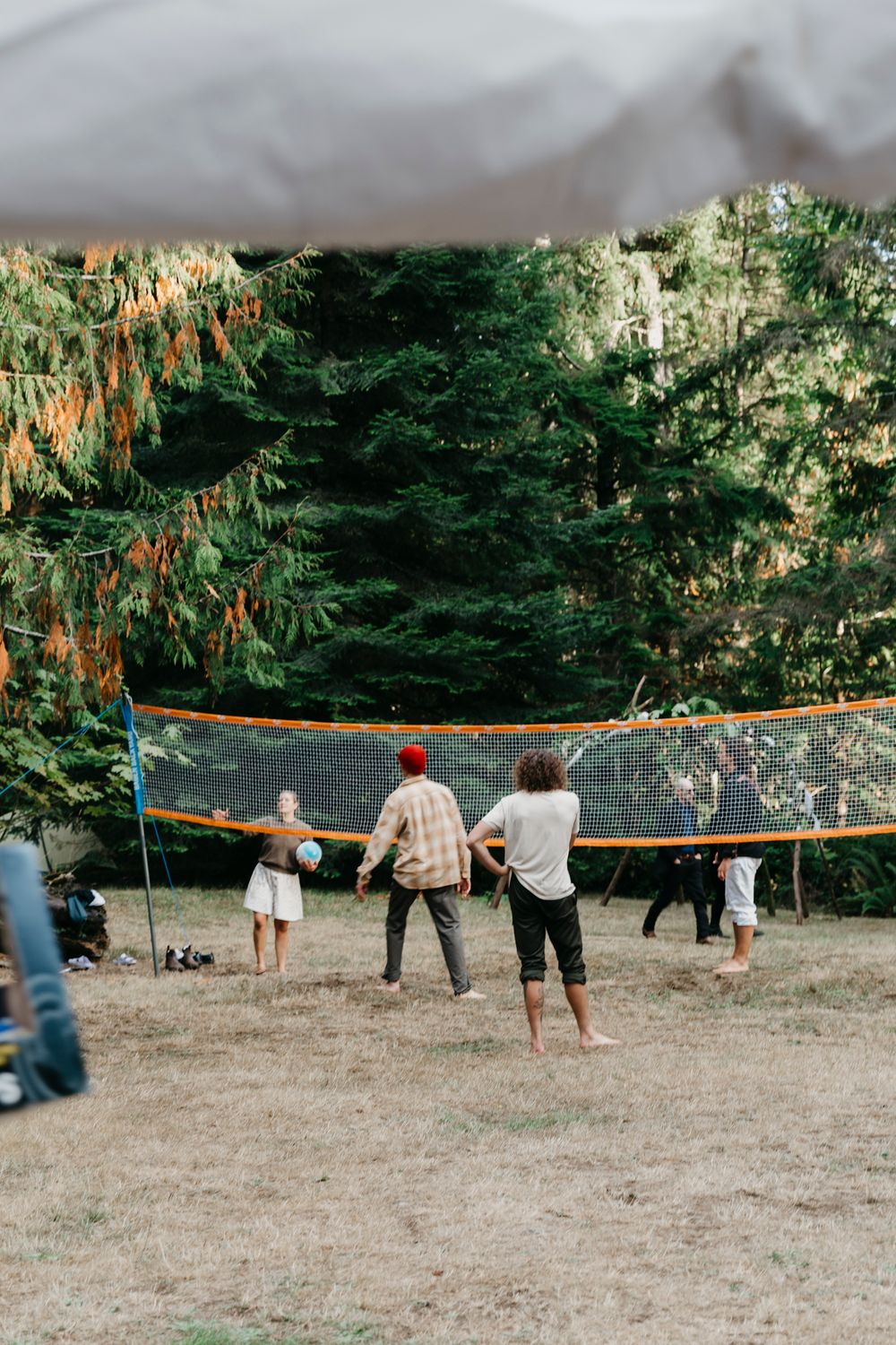 People playing volleyball outdoors in a wooded area with hanging orange lights.