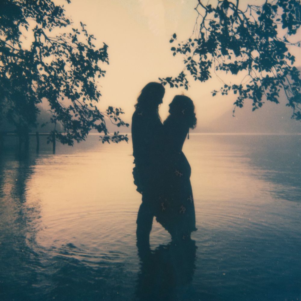 Romantic silhouettes of a couple by a lake at sunset with overhanging tree branches.