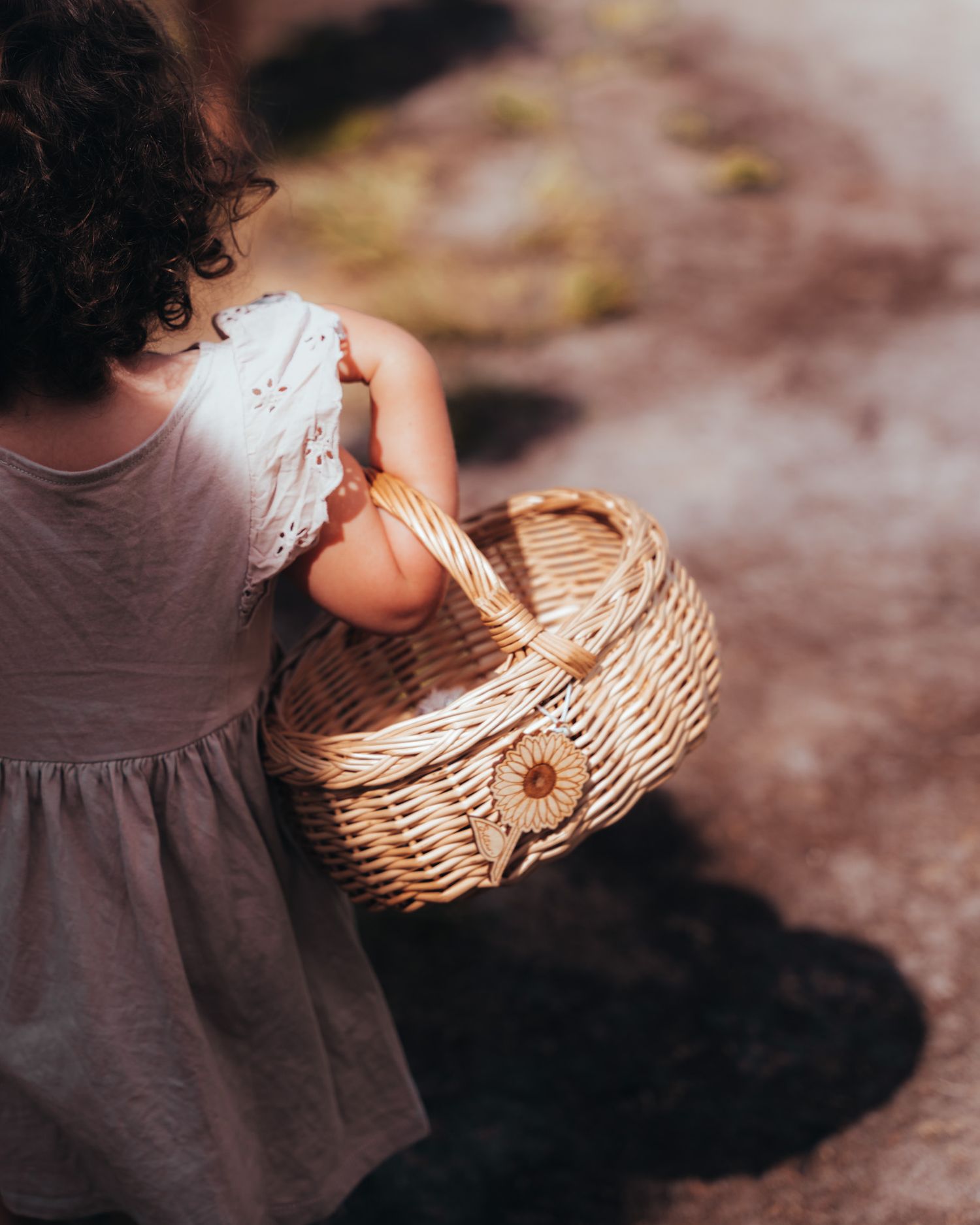 Child in purple dress holding wicker basket viewed from behind.