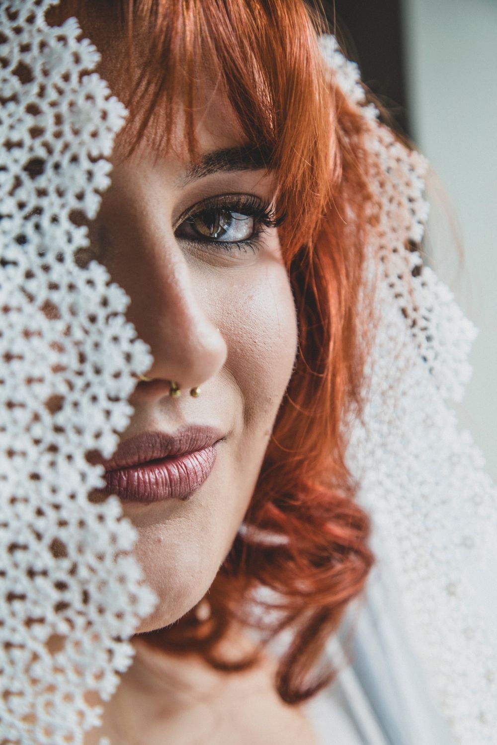 Close up portrait with delicate lace veil, vibrant red hair, burgundy lipstick and smoky eye makeup.