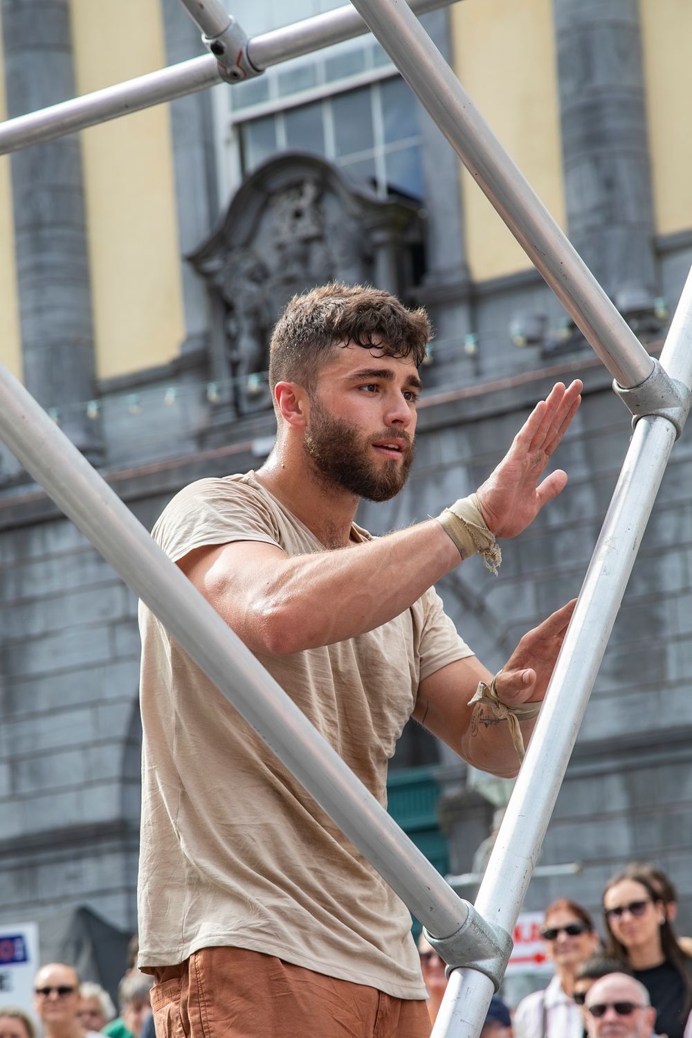 A street performer in a beige shirt stands within a metal frame structure during an outdoor performance.