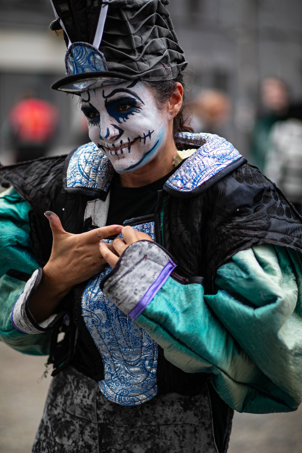 Halloween reveler in spooky skull makeup wearing ornate black and teal renaissance costume gestures at camera.