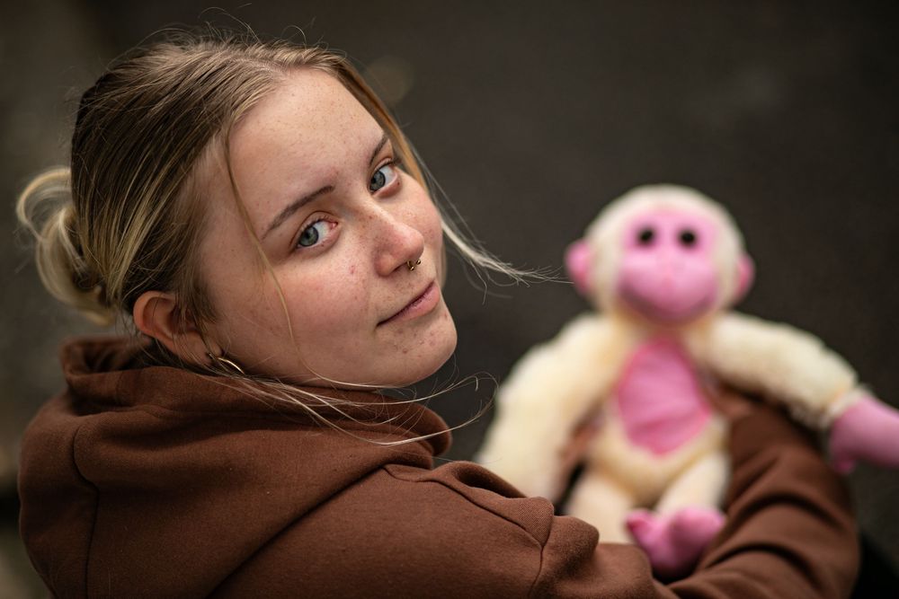 Low-light portrait with a pink plush toy in warm brown tones.