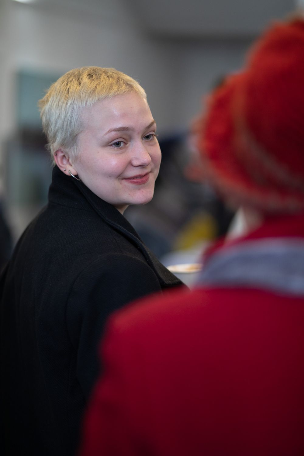 Person with short blonde hair wearing a black coat in conversation.