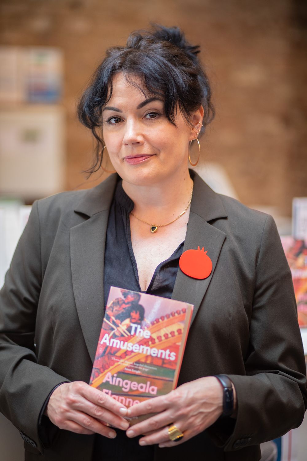 Professional in a blazer holds a book titled 'Amusements' with an orange pin on the lapel.