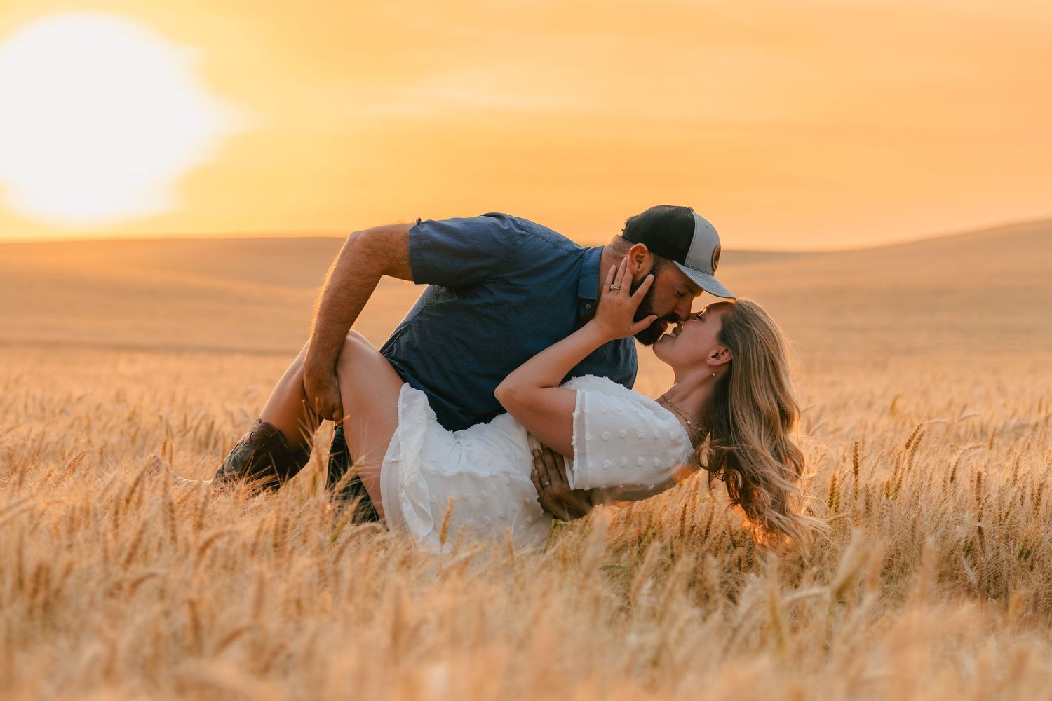 Couple sharing a romantic kiss in a golden wheat field during a stunning sunset.