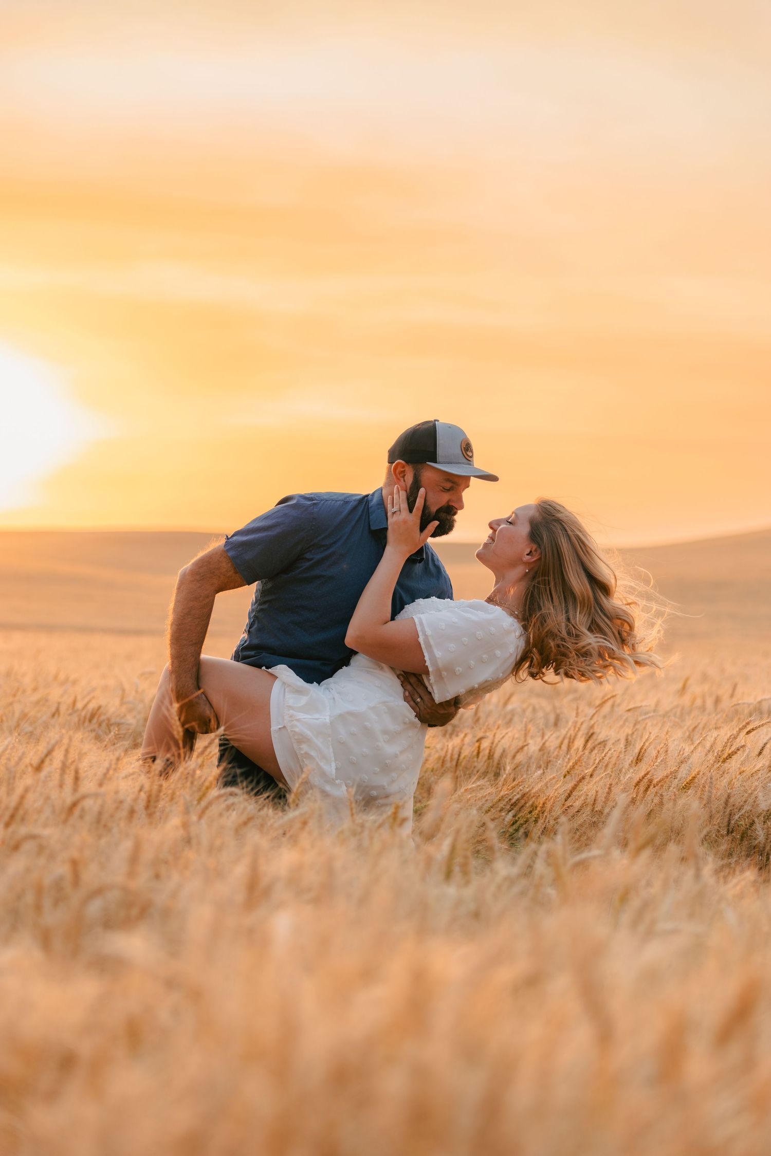 Couple sharing a romantic dip pose in a golden wheat field at sunset.