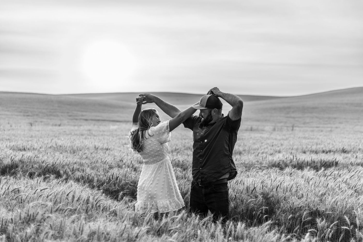 A couple dances joyfully in a vast wheat field at sunset in this romantic black and white countryside photo.