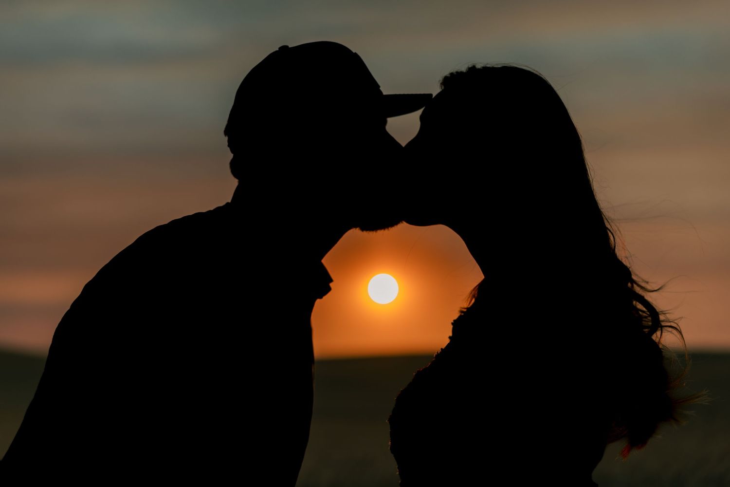Silhouette of a couple kissing at sunset with warm orange sky backdrop.