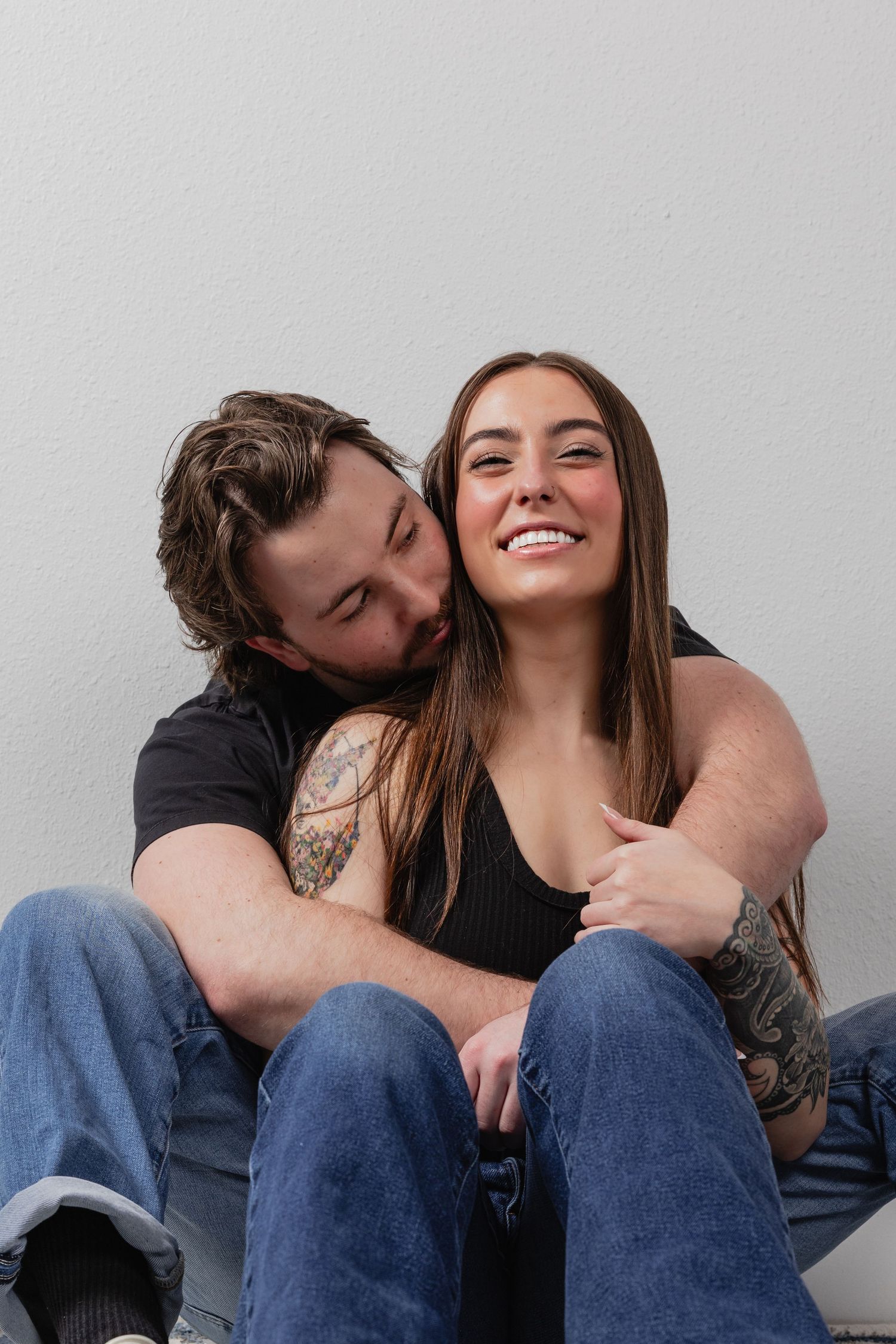 A couple in casual attire sharing intimate moments in a sequence of four candid photos against a white wall.