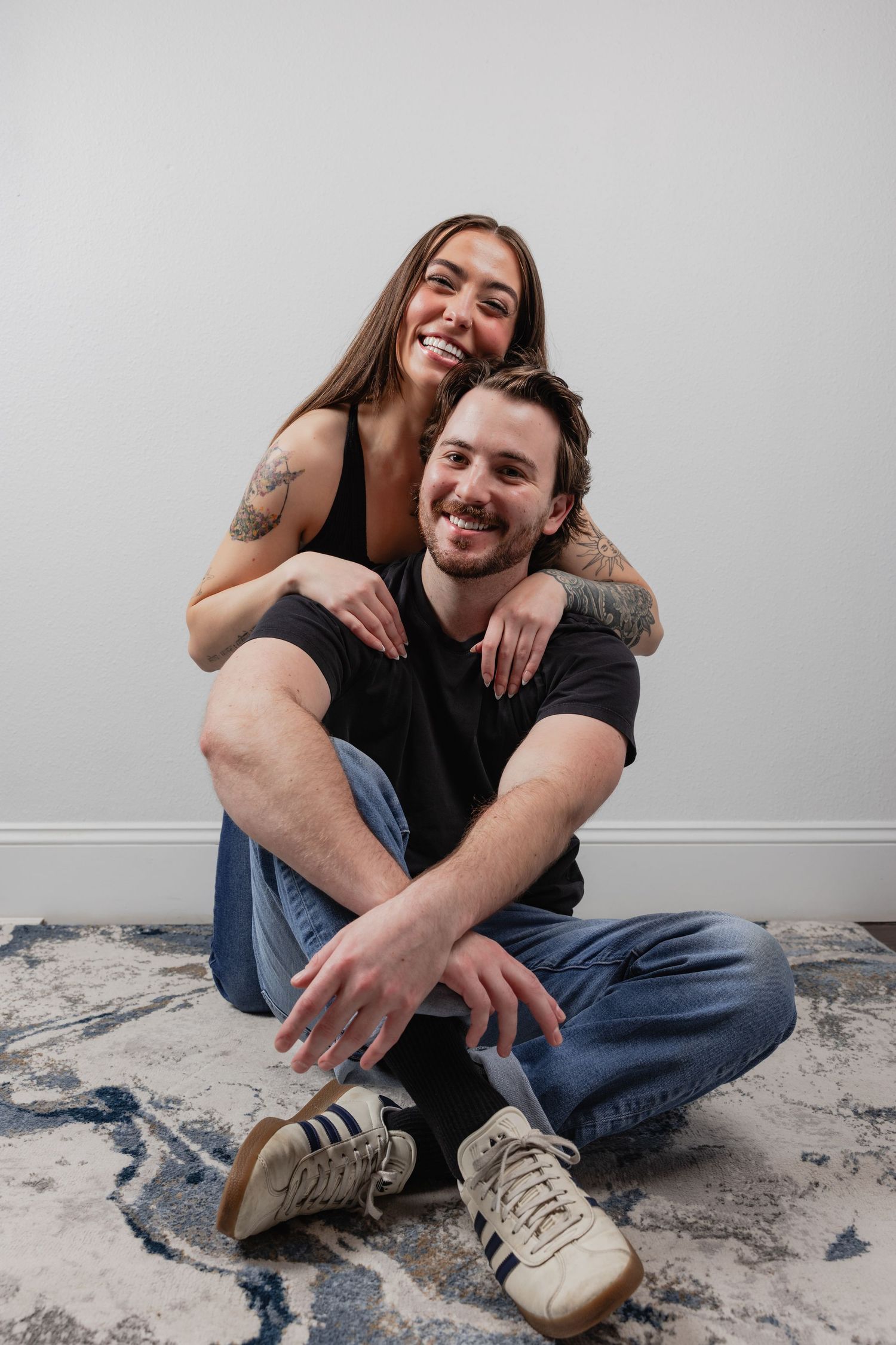 A couple sitting on a patterned rug against a white wall sharing joyful laughter together.
