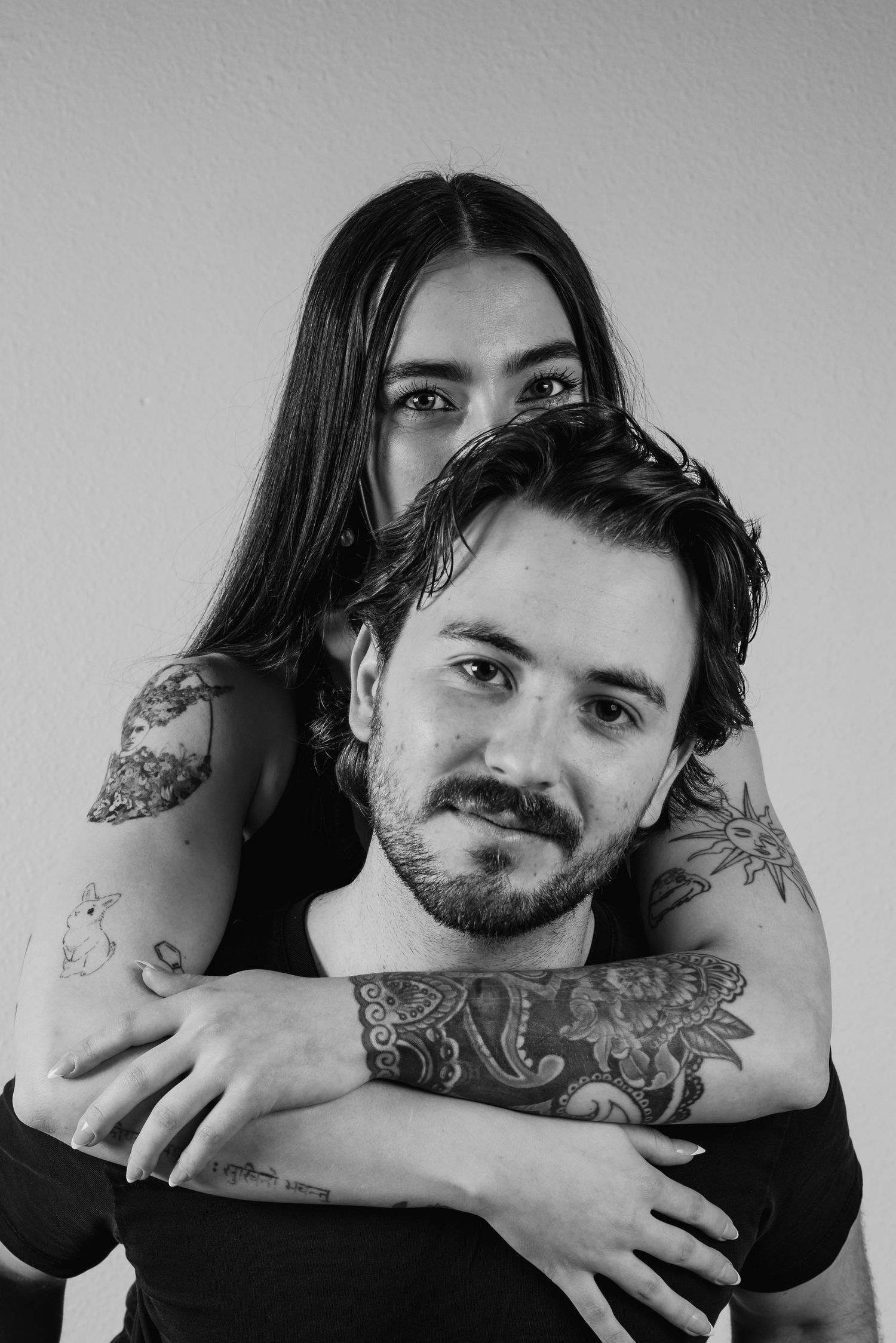 A series of black and white photographs showing a person with tattoos embracing someone in an intimate artistic pose.