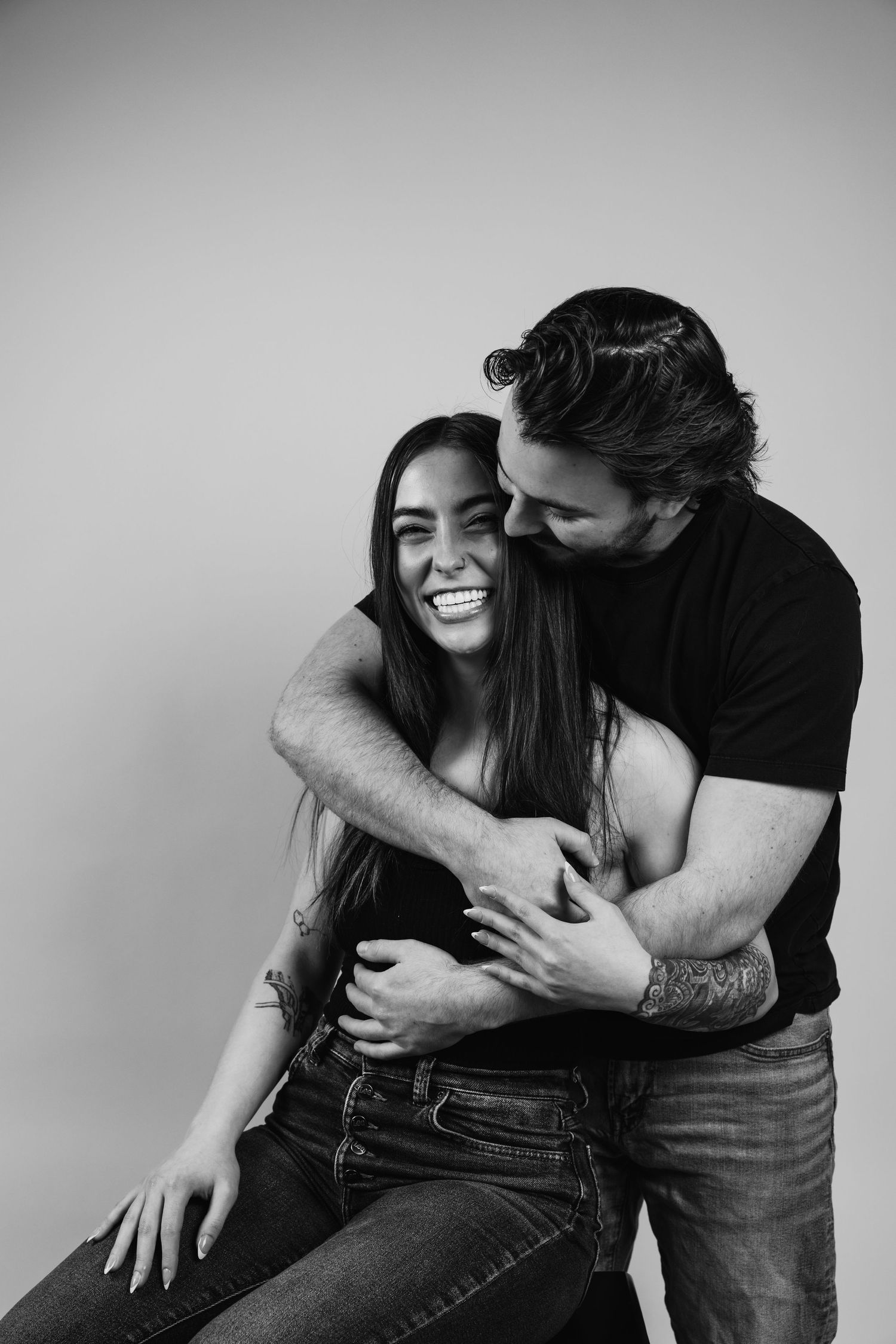 Black and white photo series showing a couple embracing and laughing together against a plain background.