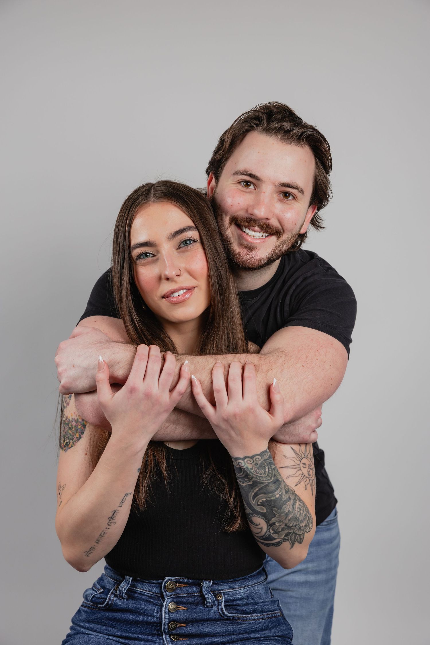 A couple in casual attire embraces and poses playfully against a gray studio backdrop in a series of candid shots.