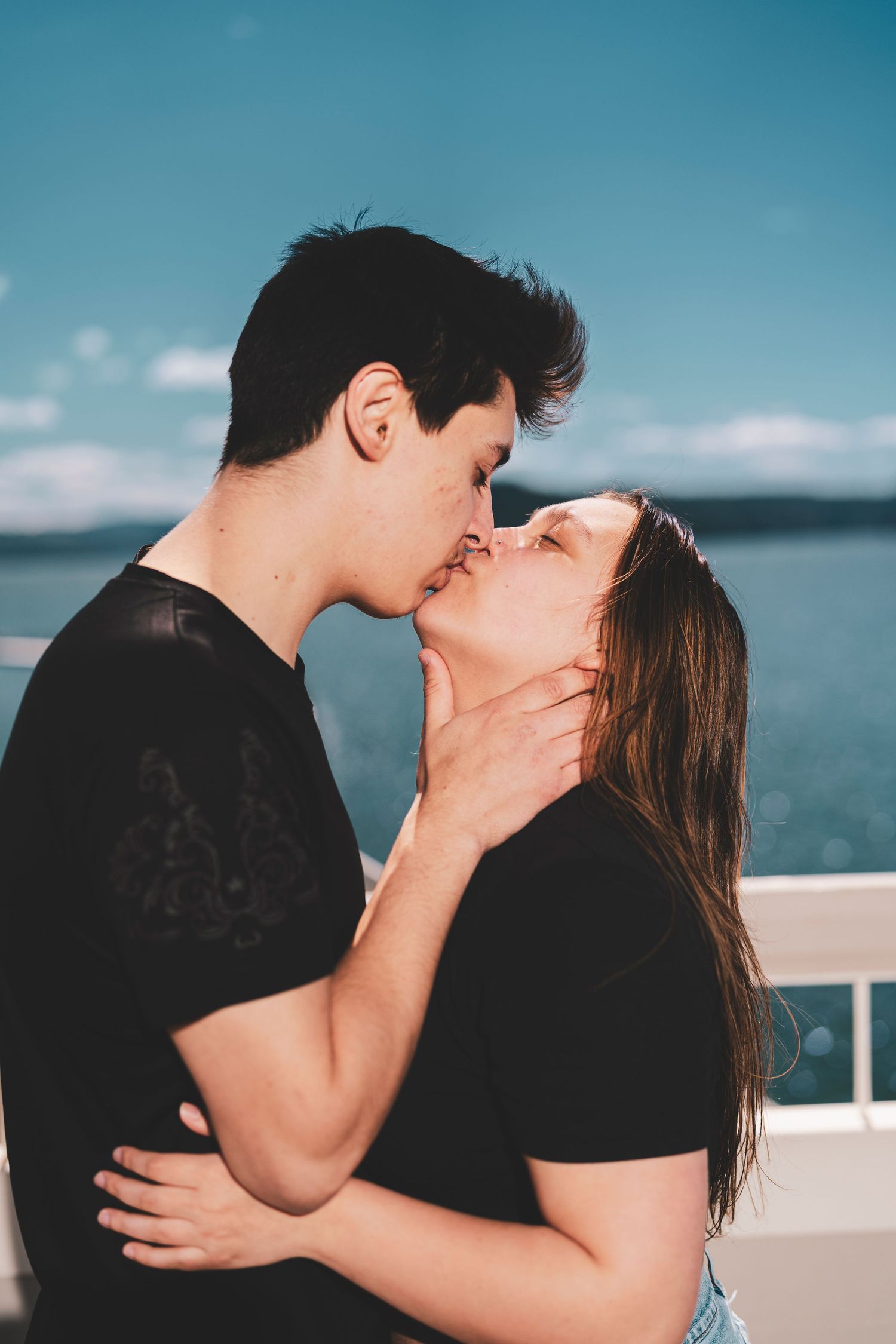 A romantic couple shares passionate kisses against a scenic ocean backdrop on a bright sunny day.