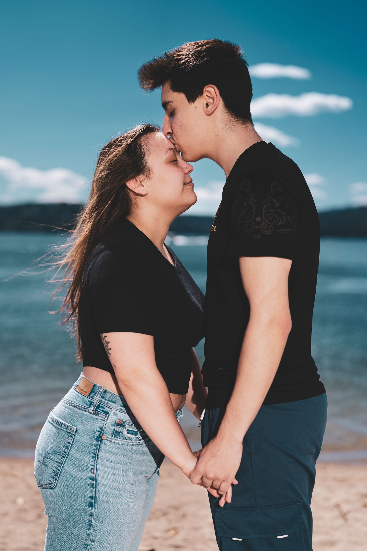 A romantic couple shares tender moments in a series of photos on a beach with blue water and sky in the background.
