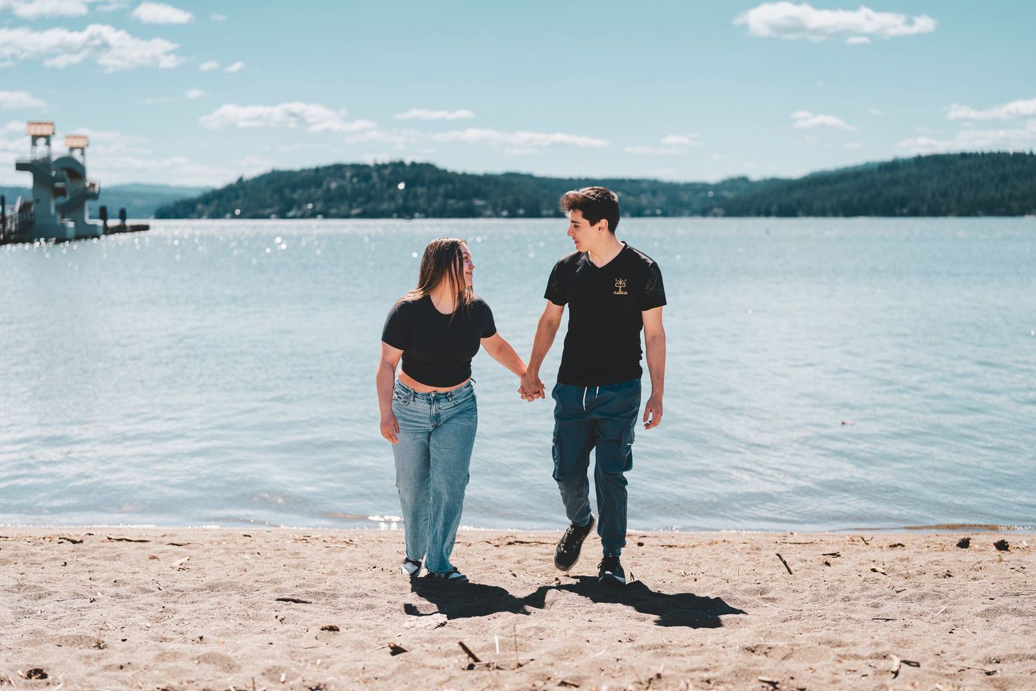 Four connected photos show people walking and sitting together on a sandy beach with a serene lake and mountains in background.