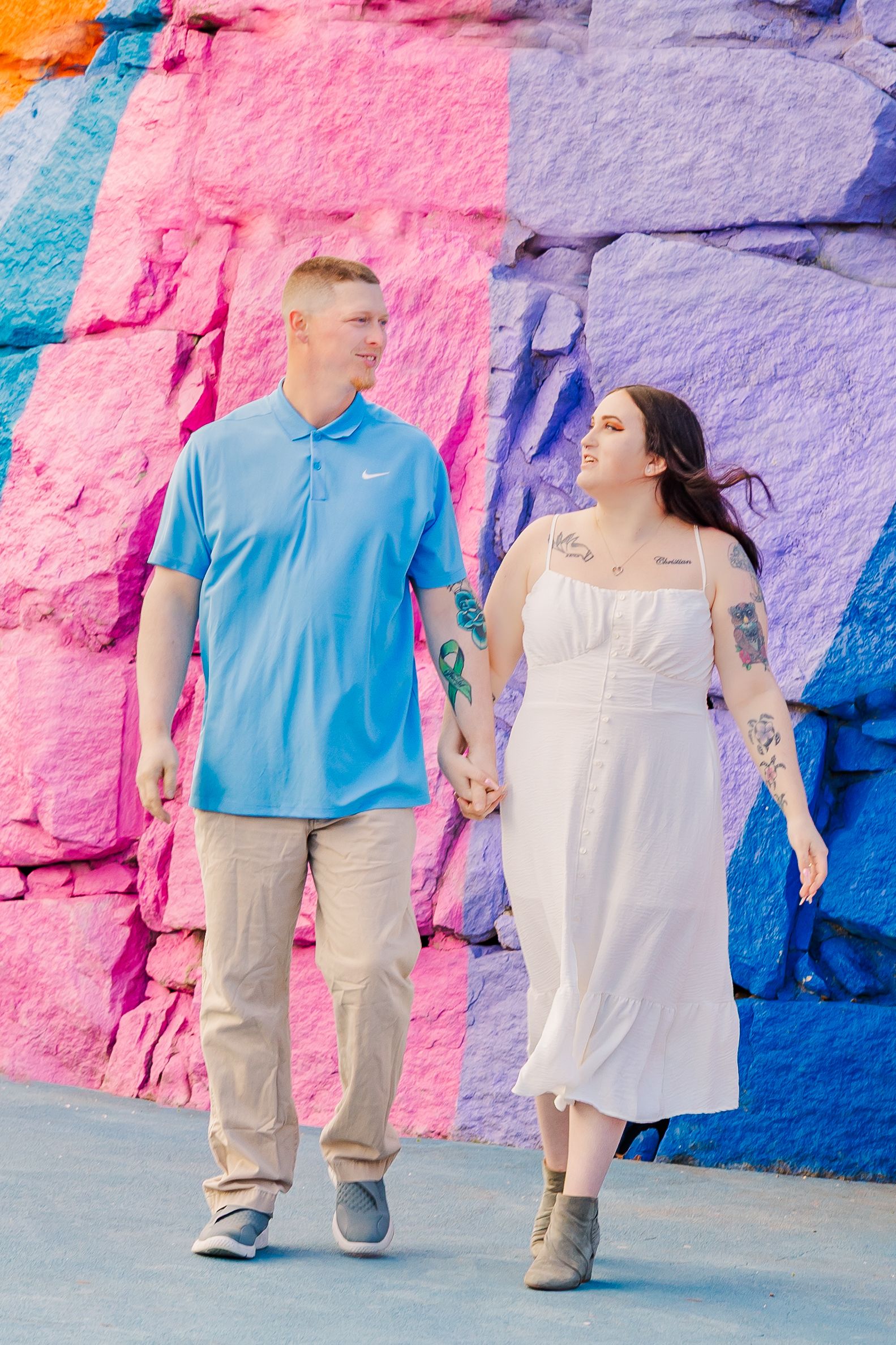 Couple walks hand in hand against colorful painted wall backdrop.