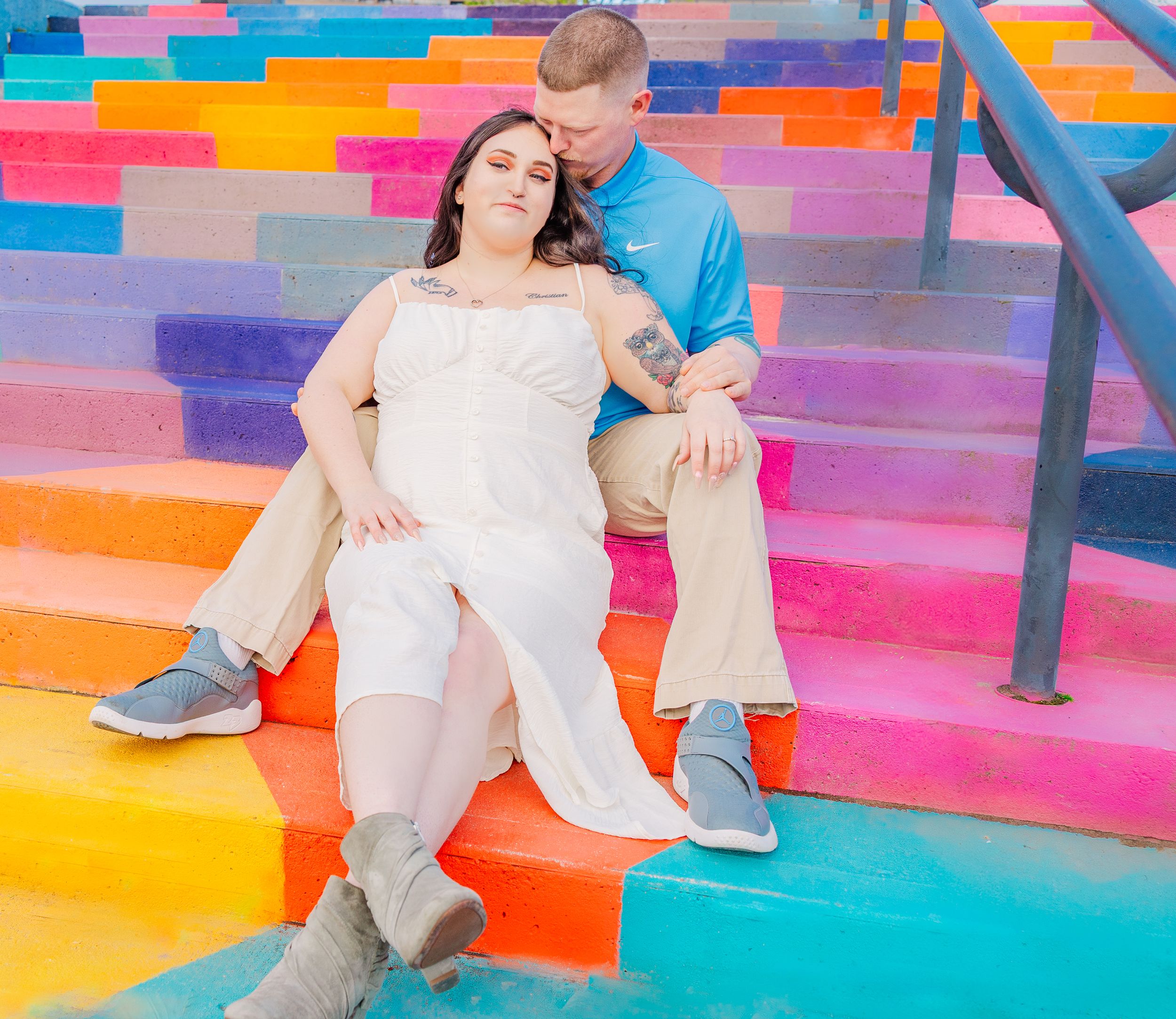 Couple lounges on rainbow painted staircase in casual yet elegant attire.