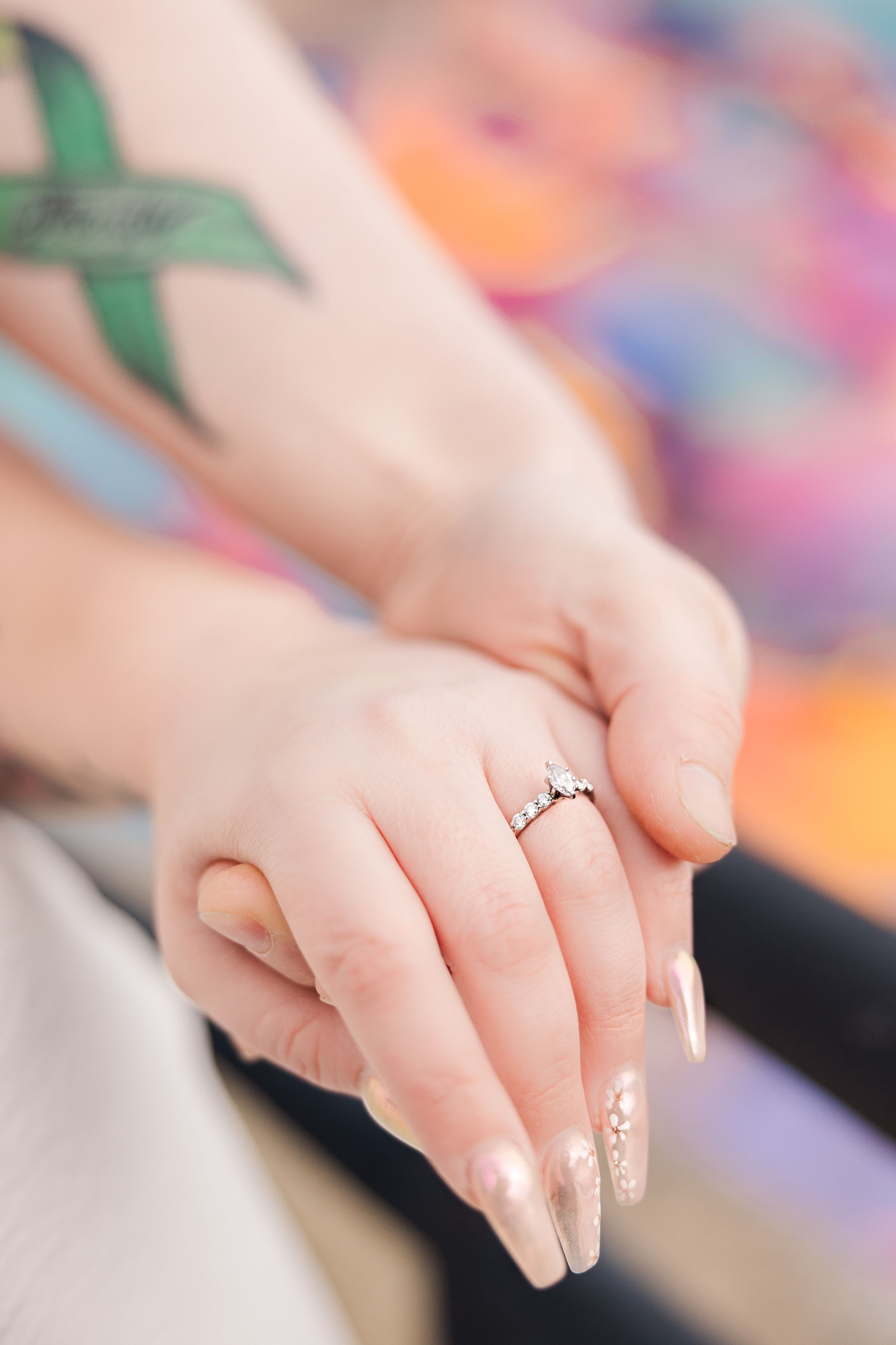 Close-up of engagement ring on woman's manicured hand with colorful background.