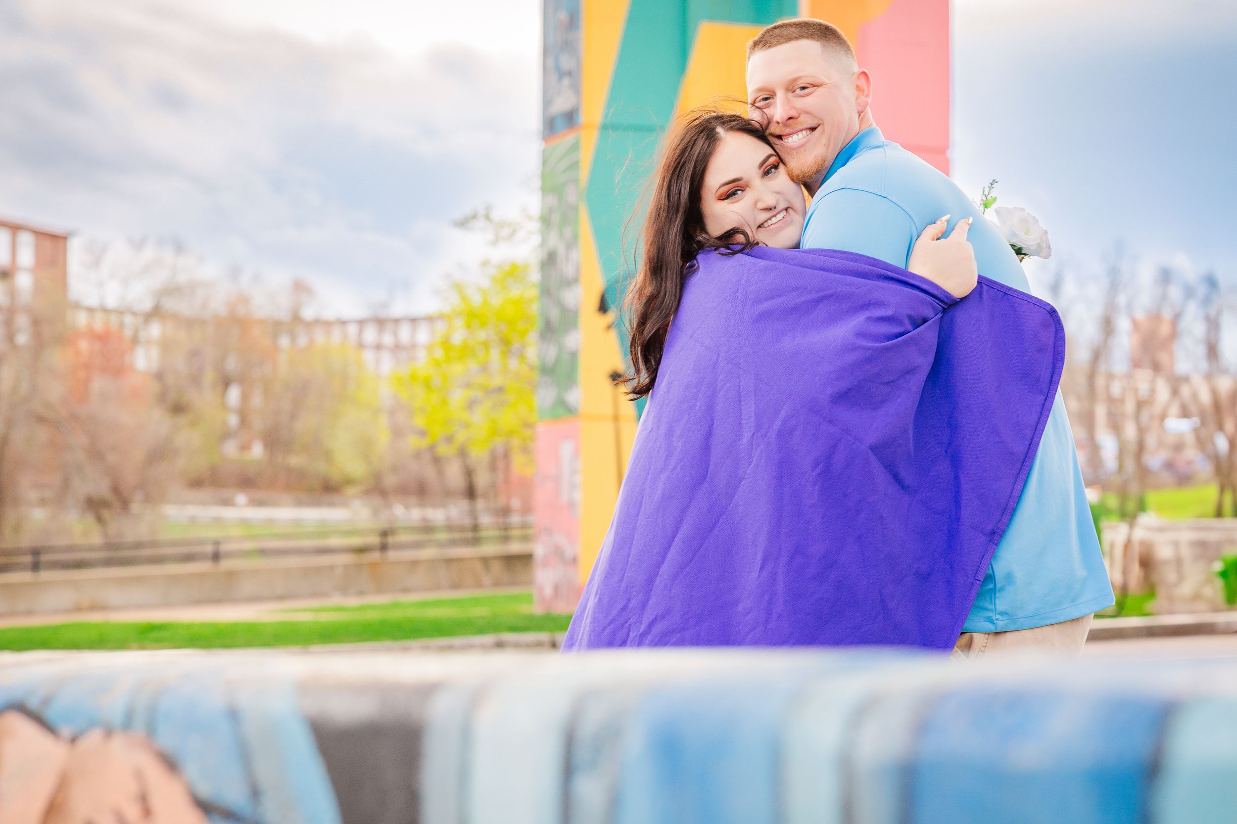 Couple embracing in purple outfits against colorful urban mural backdrop.