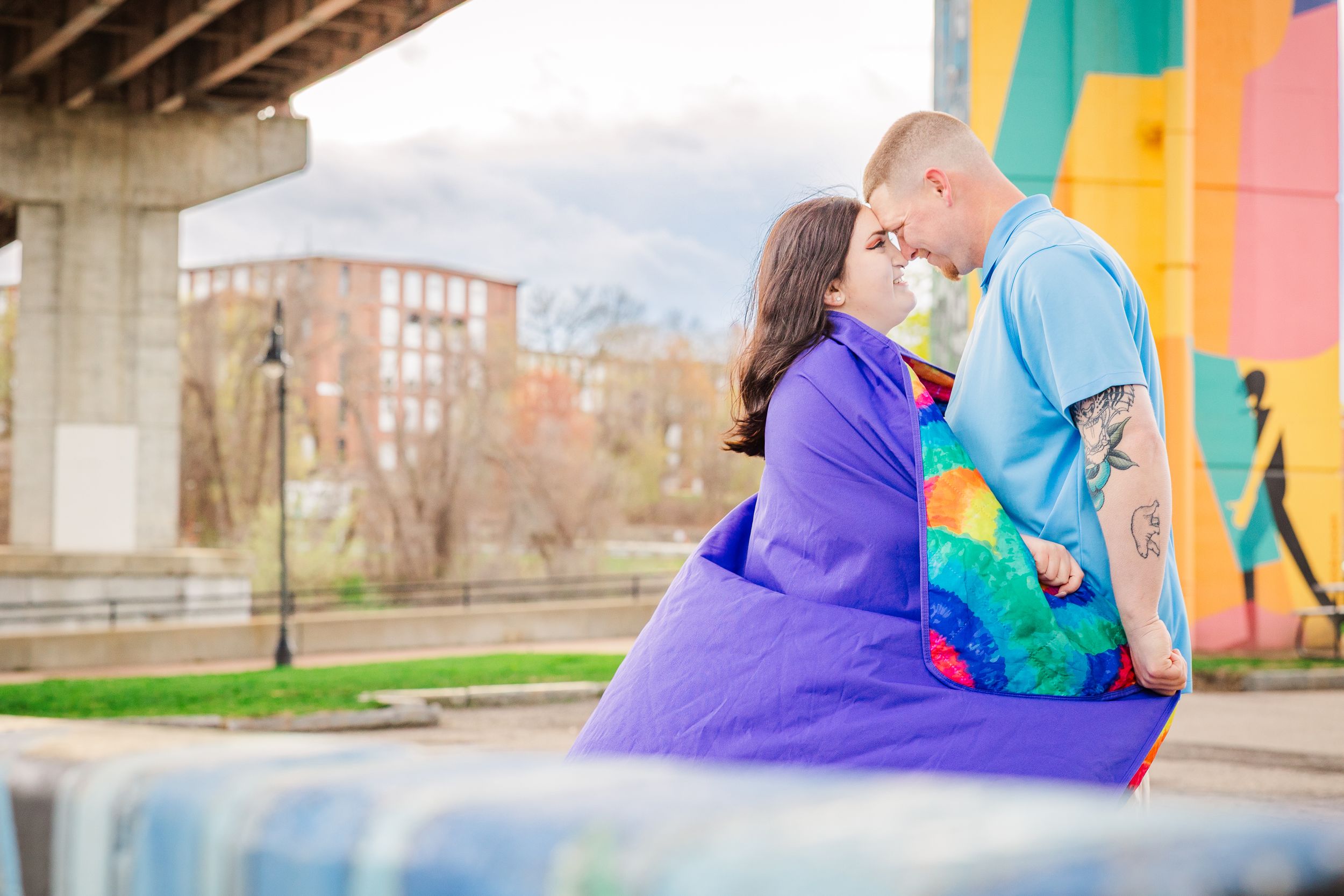 Couple sharing intimate moment in front of bright street art wall wearing matching purple outfits.