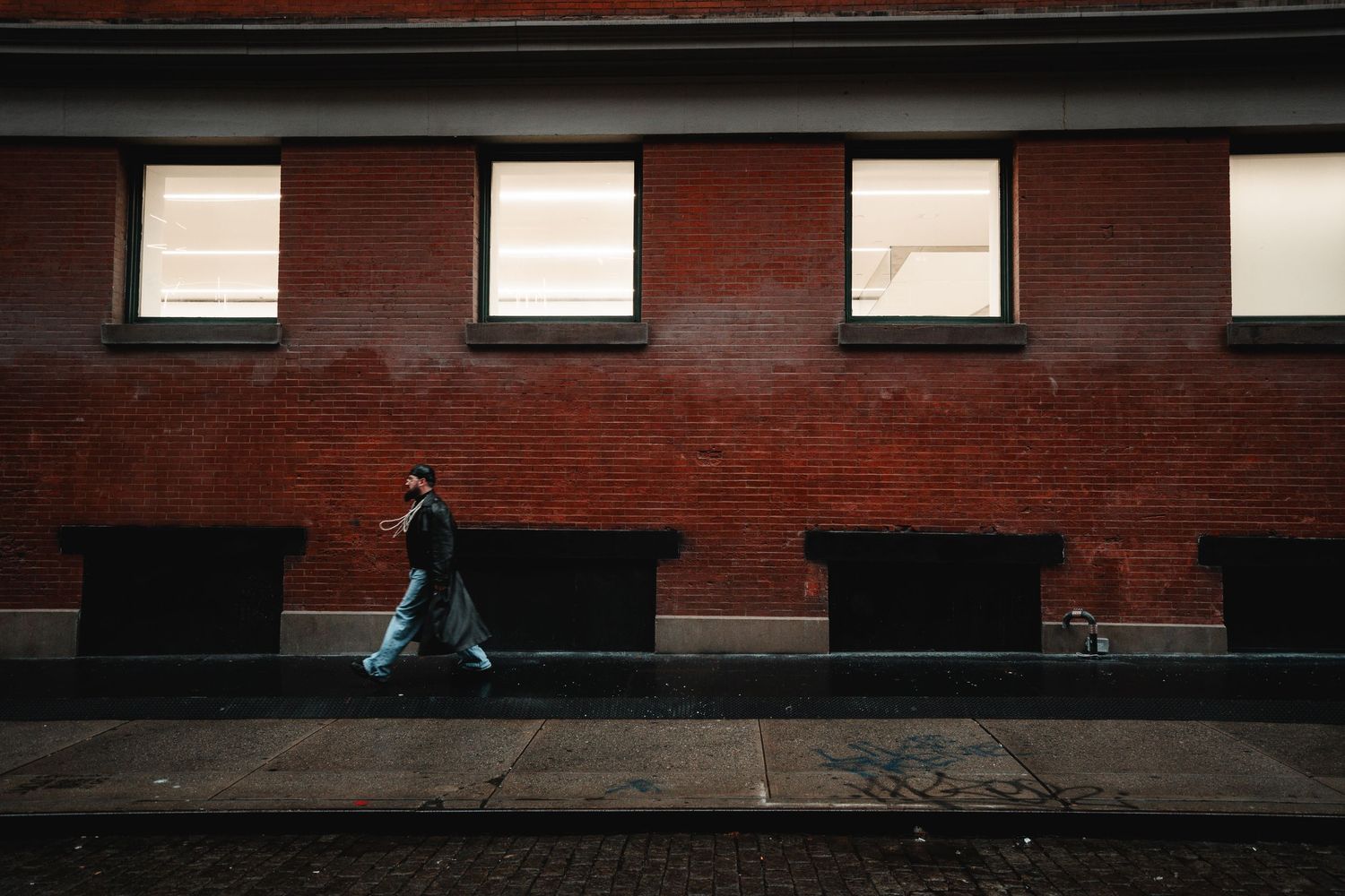 Person walking past a brick building with row of small windows on an urban street.