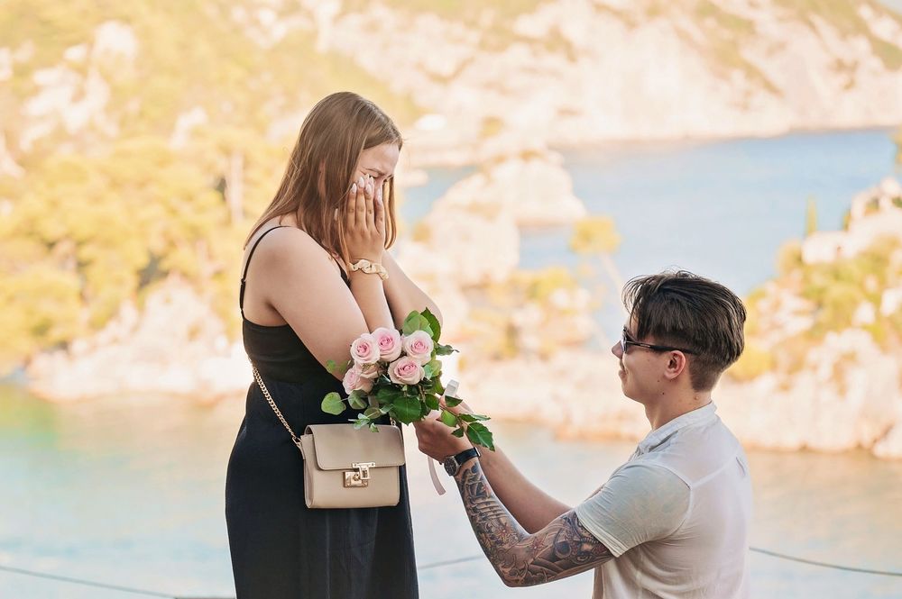 Surprise proposal moment with flowers against stunning coastal background.