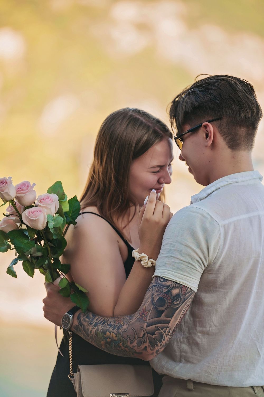 A romantic moment with pink roses as a couple shares an intimate embrace in warm sunlight.