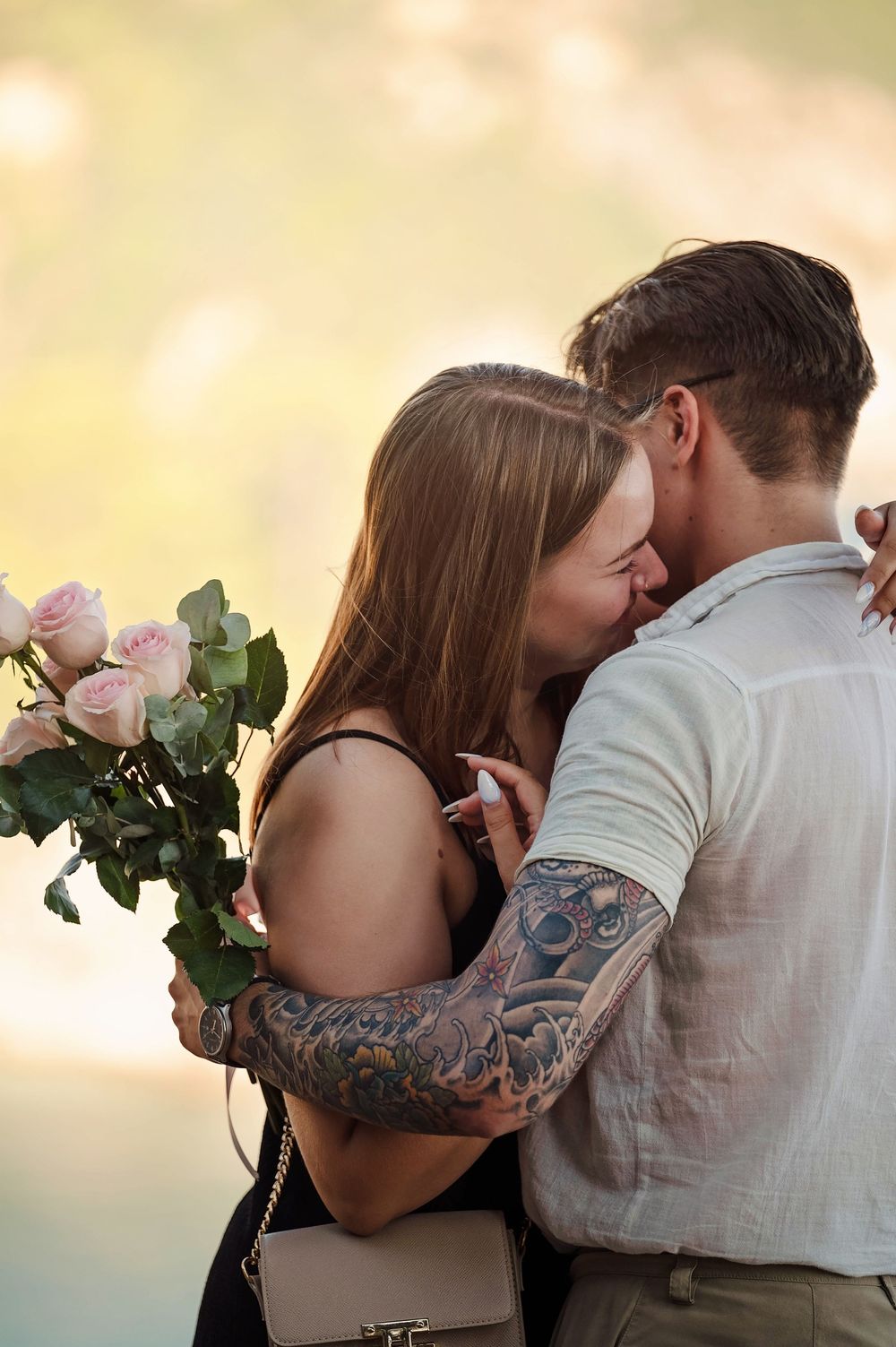 Newly engaged couple sharing romantic moment with bouquet against coastal sunset.