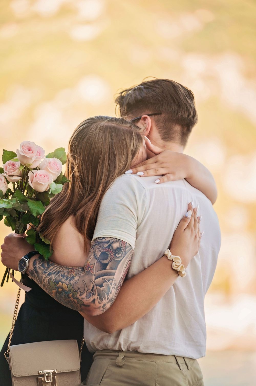 Couple embracing with pink roses and a beige purse during a tender moment outdoors.
