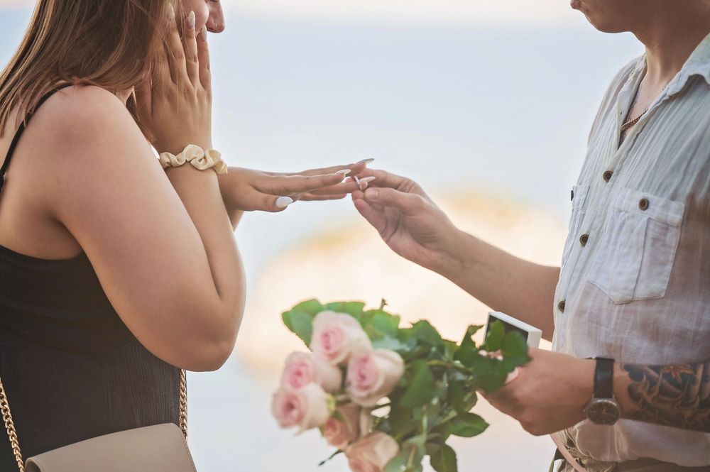 A close-up of hands during a romantic proposal with pink roses in the foreground.