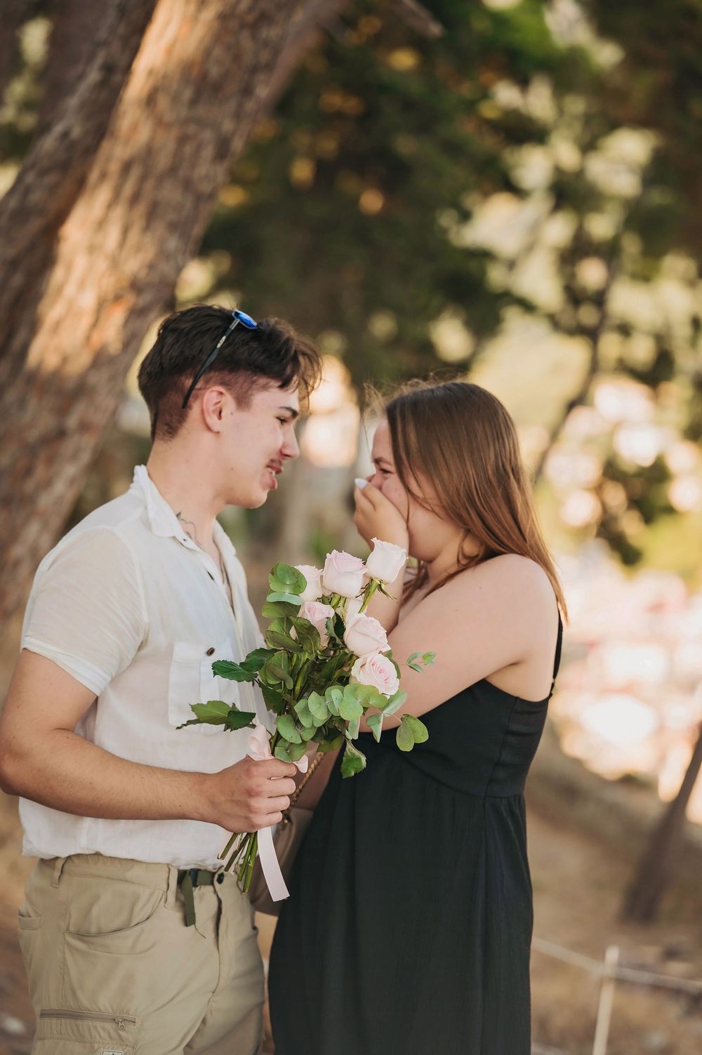 A romantic scene with pink roses as a couple shares a sweet moment under trees.