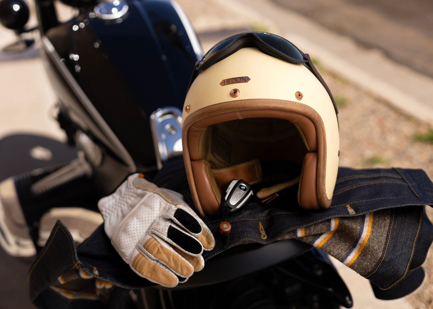 Vintage cream motorcycle helmet and leather gloves resting on black motorcycle seat.