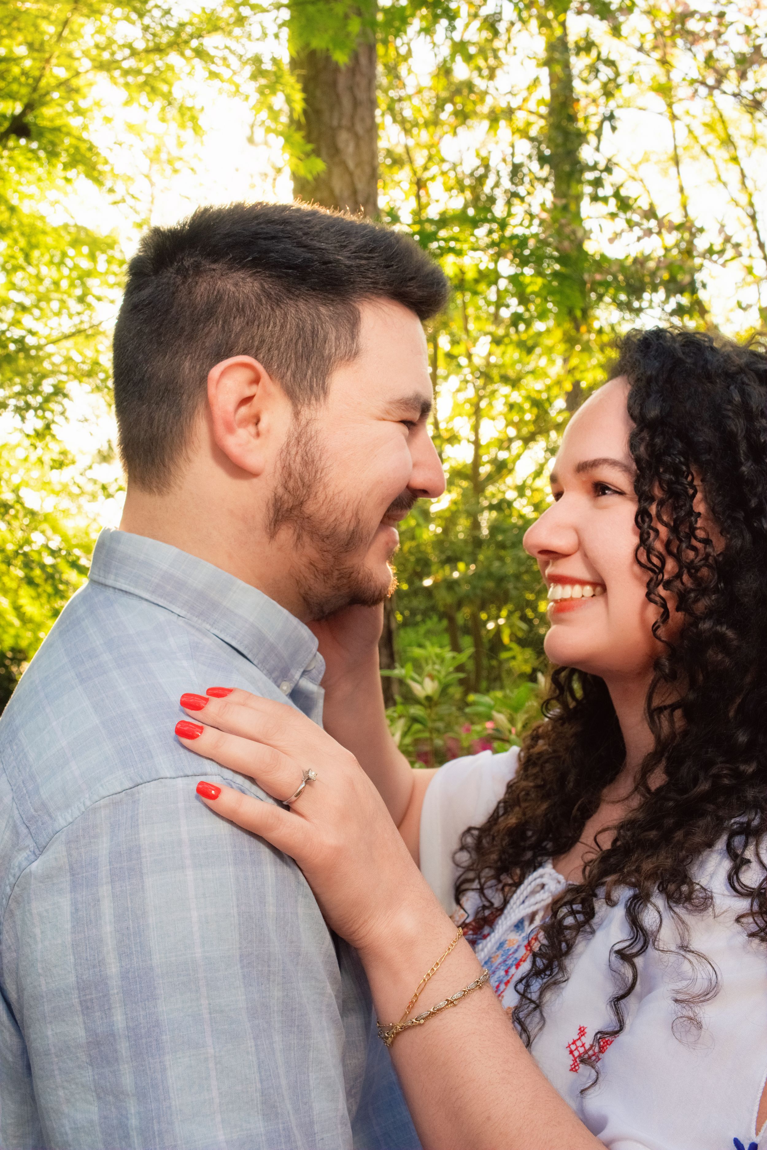 Romantic couple embraces in a sunny woodland setting with natural sunlight filtering through green trees.