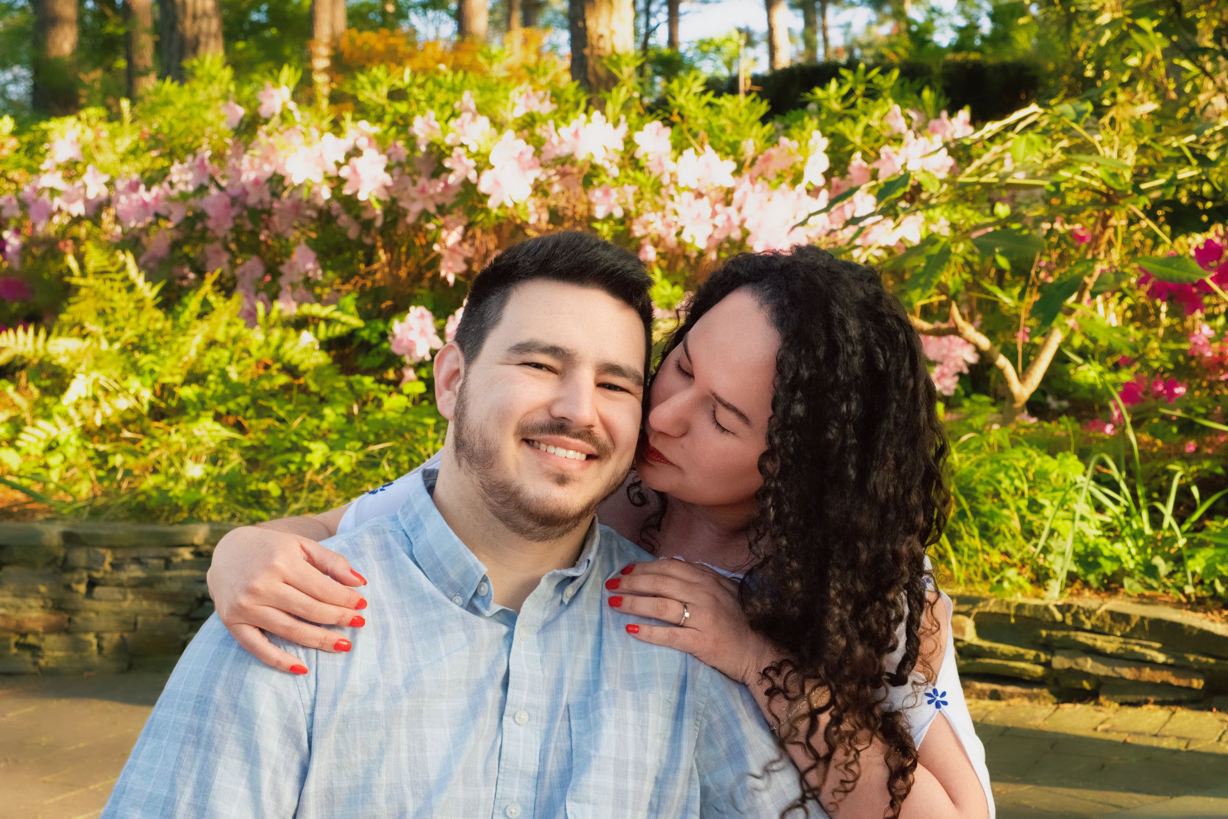 A happy couple embraces outdoors in a garden with colorful flowers and greenery in the background.