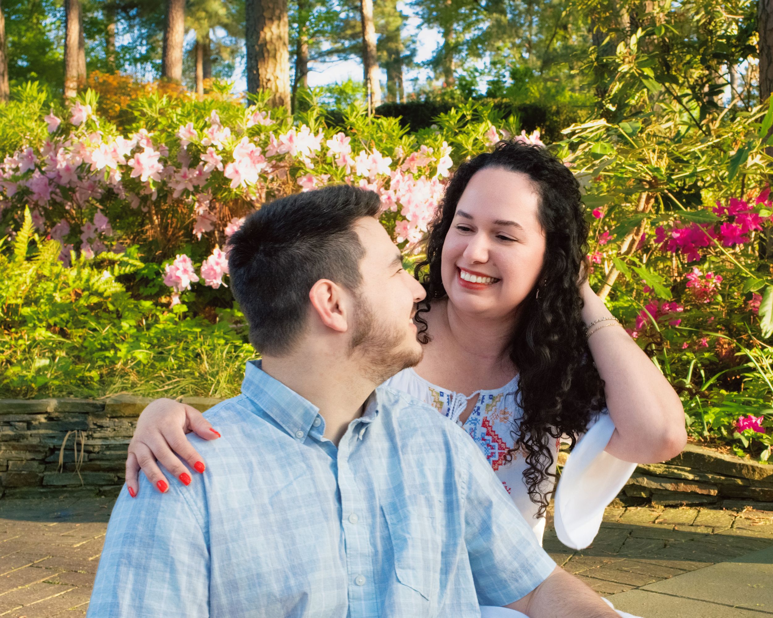 A couple shares a joyful moment together in a vibrant garden filled with colorful flowers and tall trees.