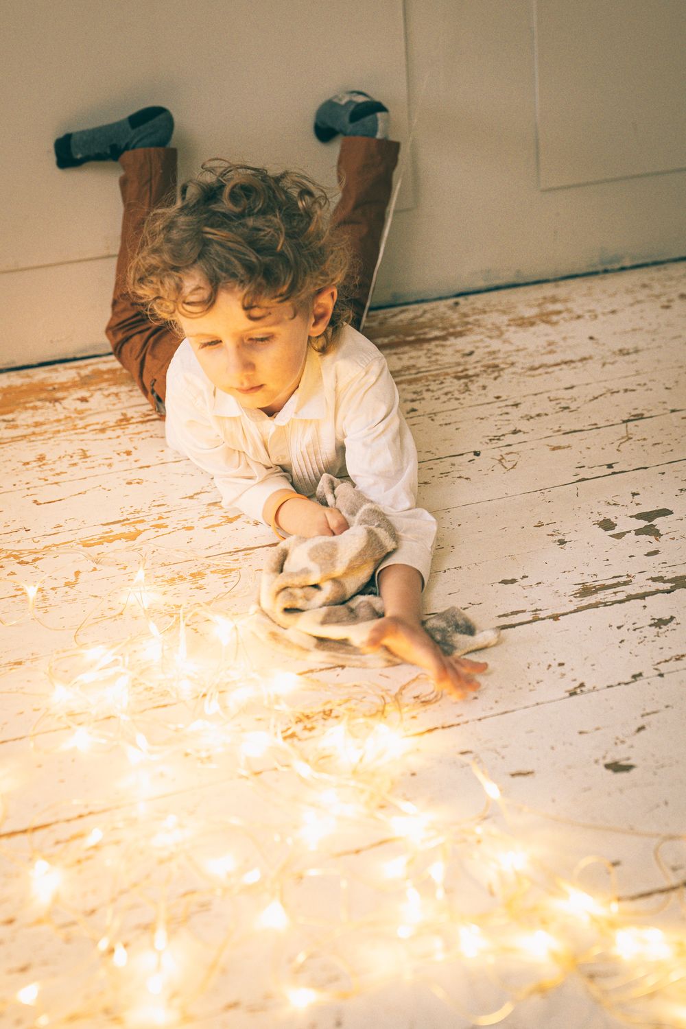 A child lies on a white wooden floor surrounded by glowing string lights creating a magical atmosphere.