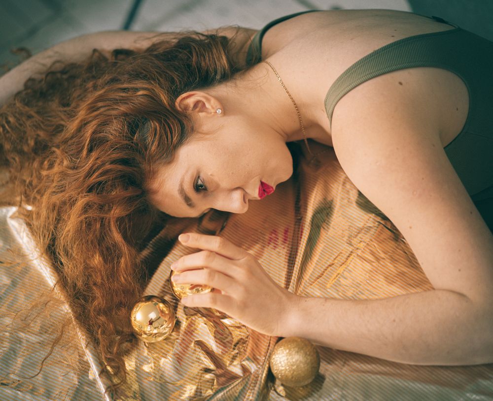 Artistic portrait with person lying on gold fabric with Christmas ornaments.