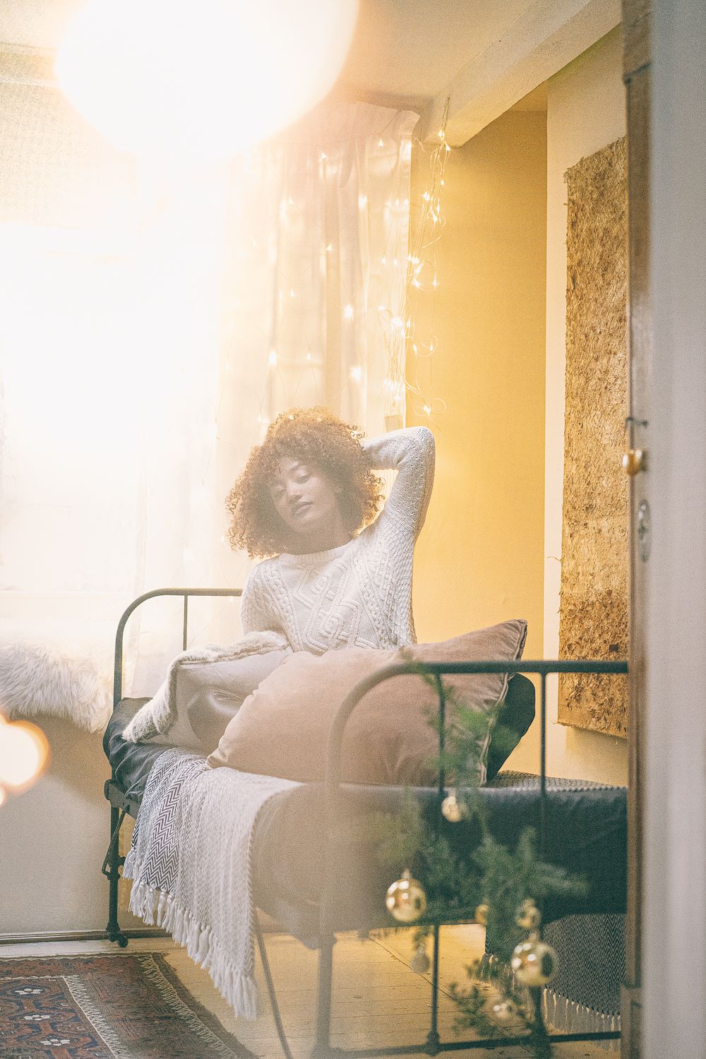 Person relaxing on bed with white bedding and hanging lights creating dreamy atmosphere.