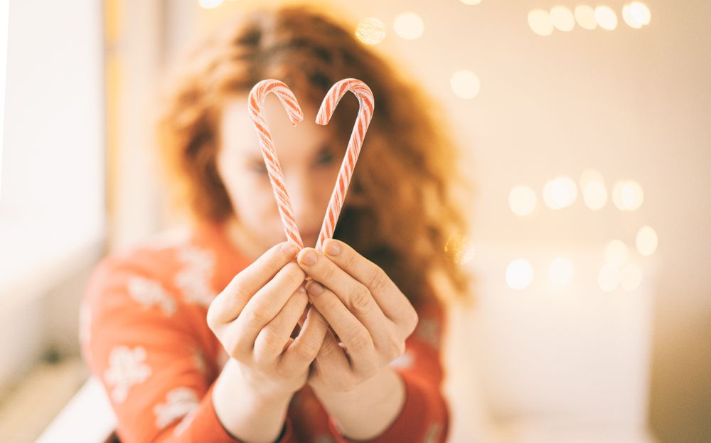 Hands holding candy canes forming heart shape with bokeh lights in background.