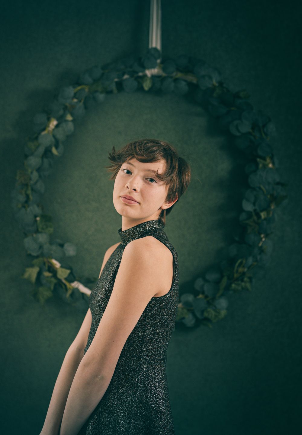 Portrait of person in dark sleeveless dress posing against green wall with floral arch.