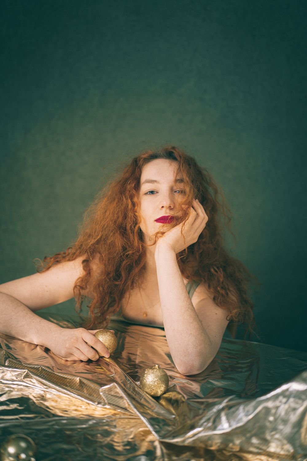 Portrait of someone with flowing red hair posing against a dark green background with holiday decorations.