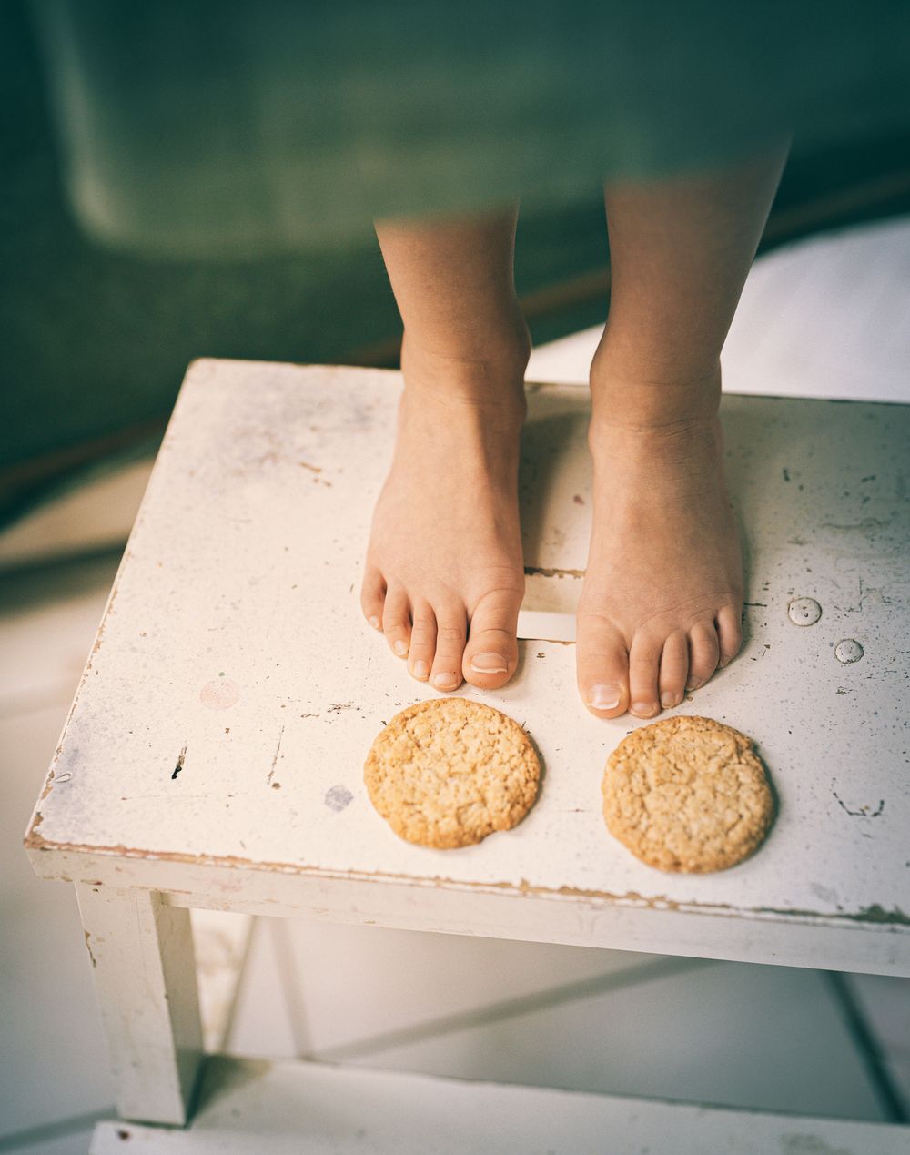 Bare feet on white table next to two round sugar cookies.