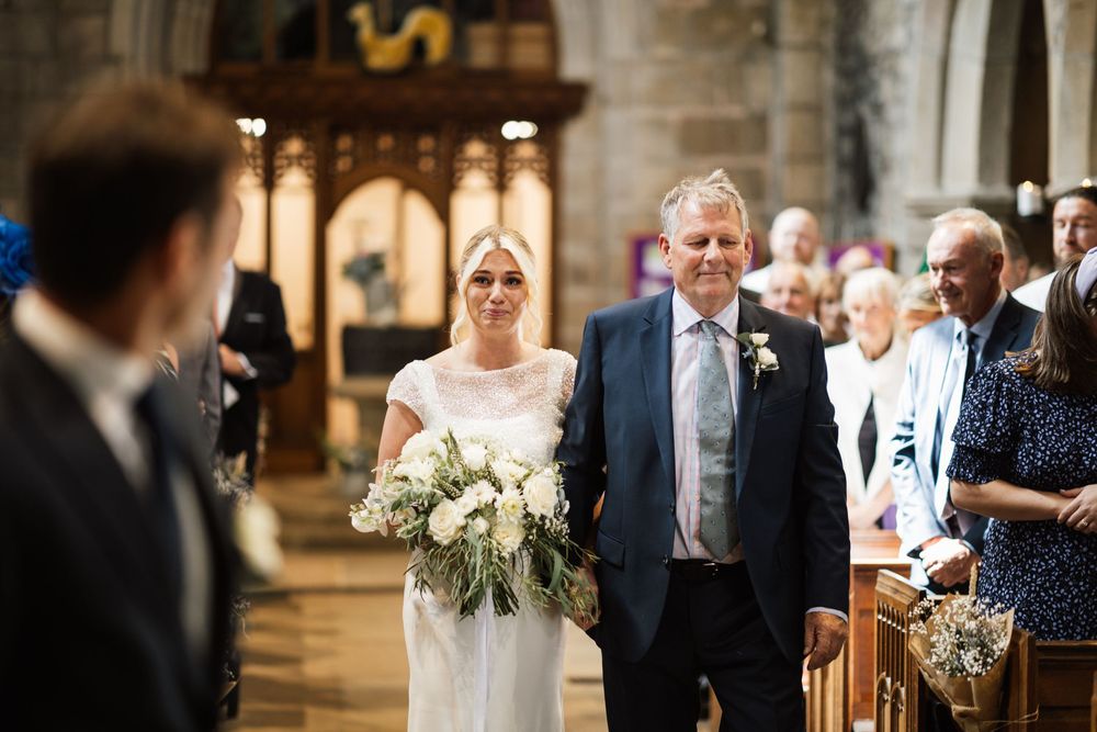 Wedding ceremony in a beautiful stone church with elegant floral arrangements and natural light streaming through windows.