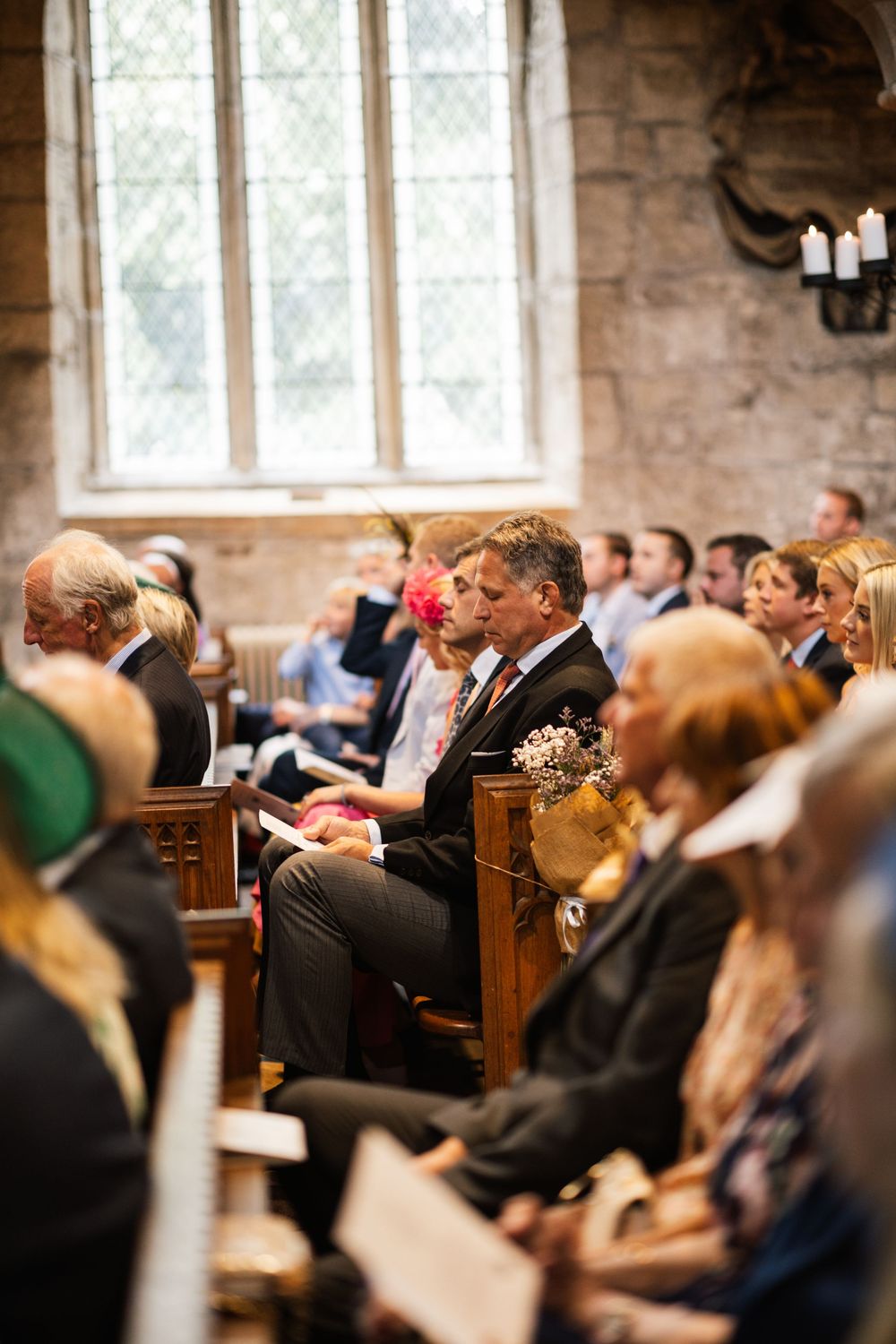 A congregation sits in wooden pews during a church service in a stone-walled sanctuary with arched windows.
