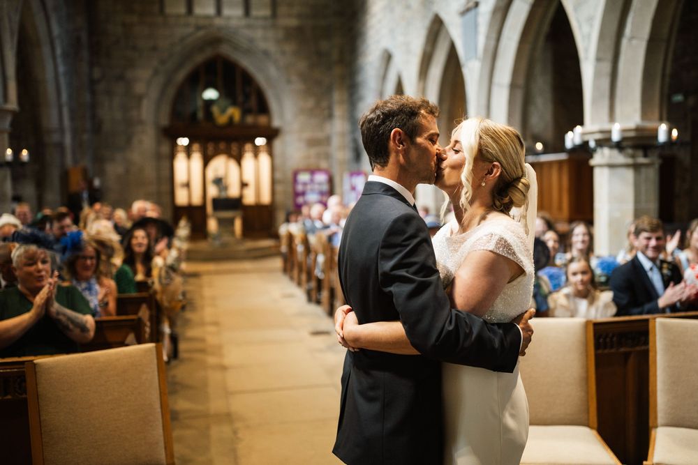 Couple shares intimate moments during their wedding ceremony in a grand cathedral with stone archways and wooden pews.