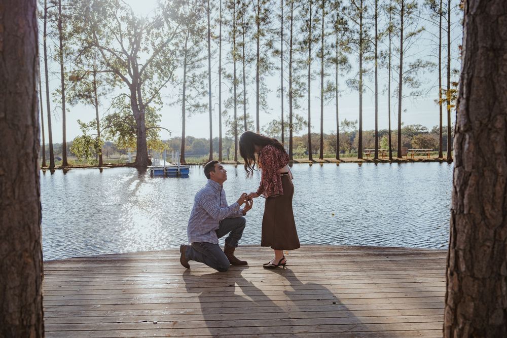 A romantic couple shares tender moments on a wooden dock overlooking a serene lake surrounded by tall pine trees.